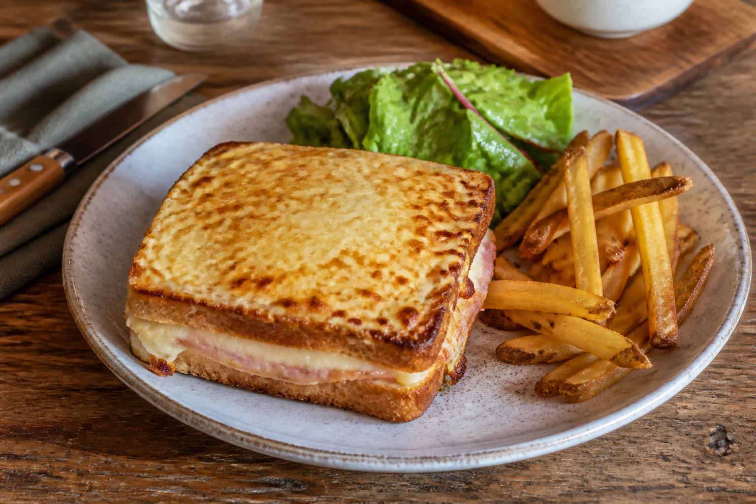 Croque-monsieur gratiné servi avec une salade verte et des frites maison sur une table en bois